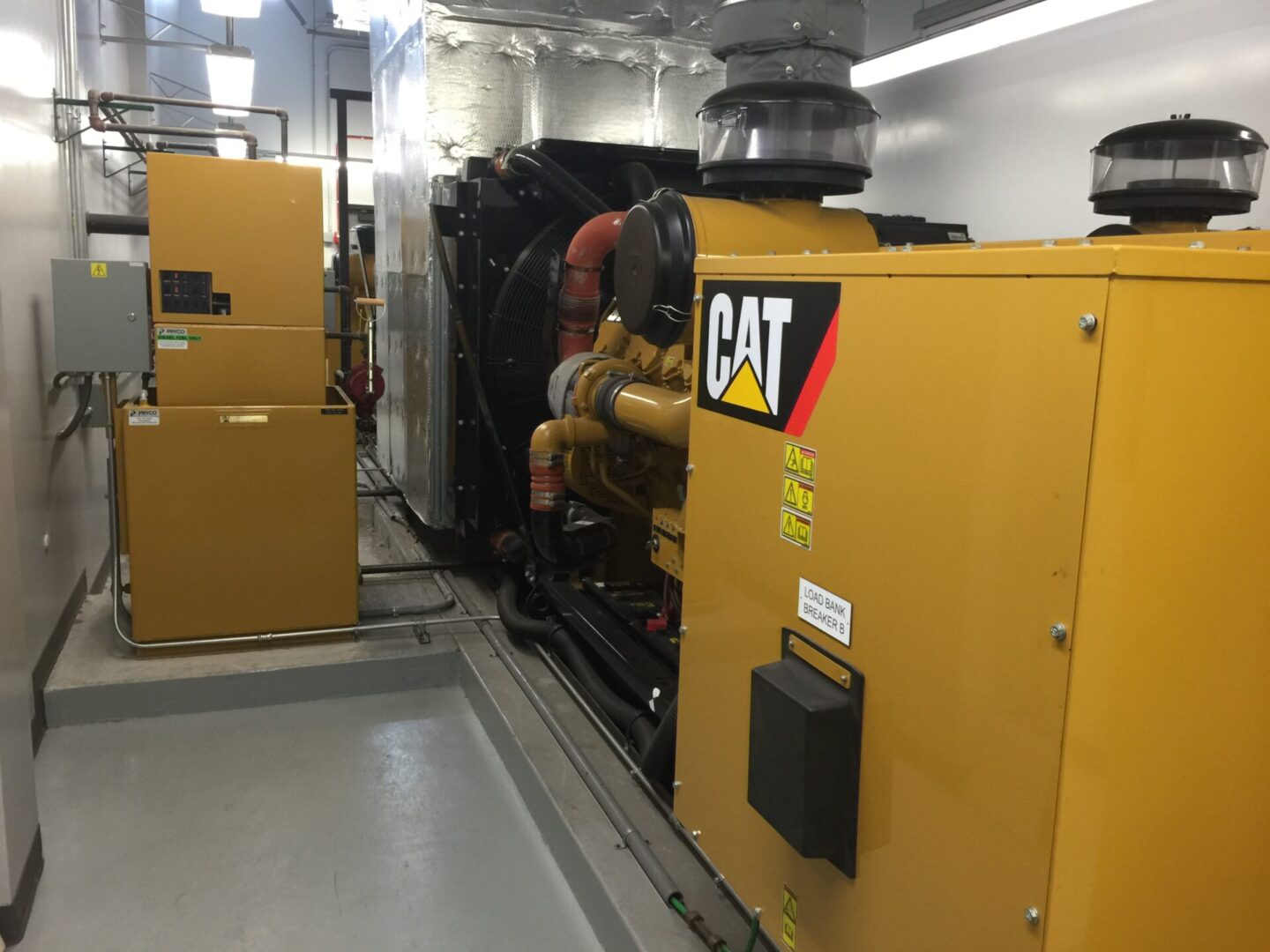 Yellow CAT heavy equipment with cylindrical tubes attached to a wall-sized ventilation fan