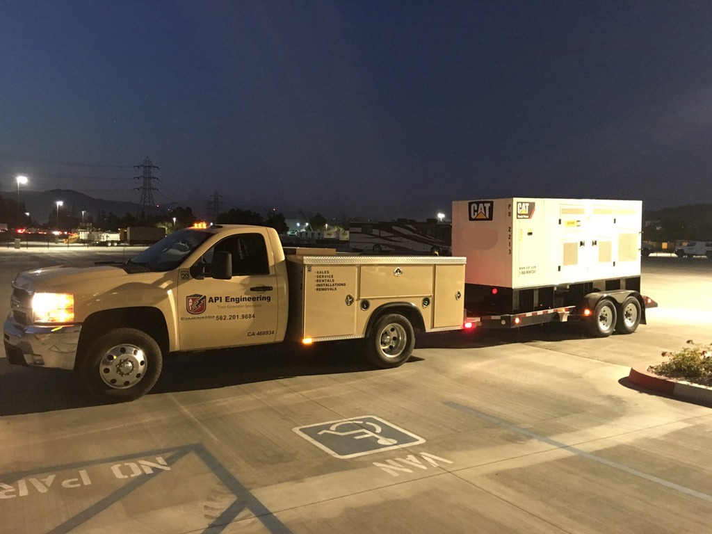 Cream-colored pickup truck towing a white CAT generator during night time