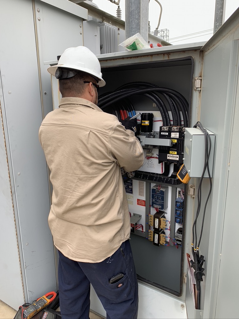 Man in a beige jacket inspecting the cable wires of a white generator’s control panel