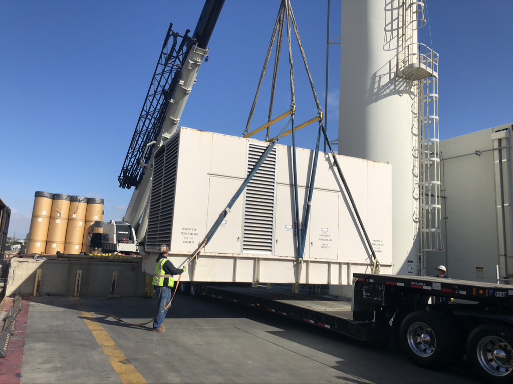 Huge white generator being lifted up from a truck trailer attachment