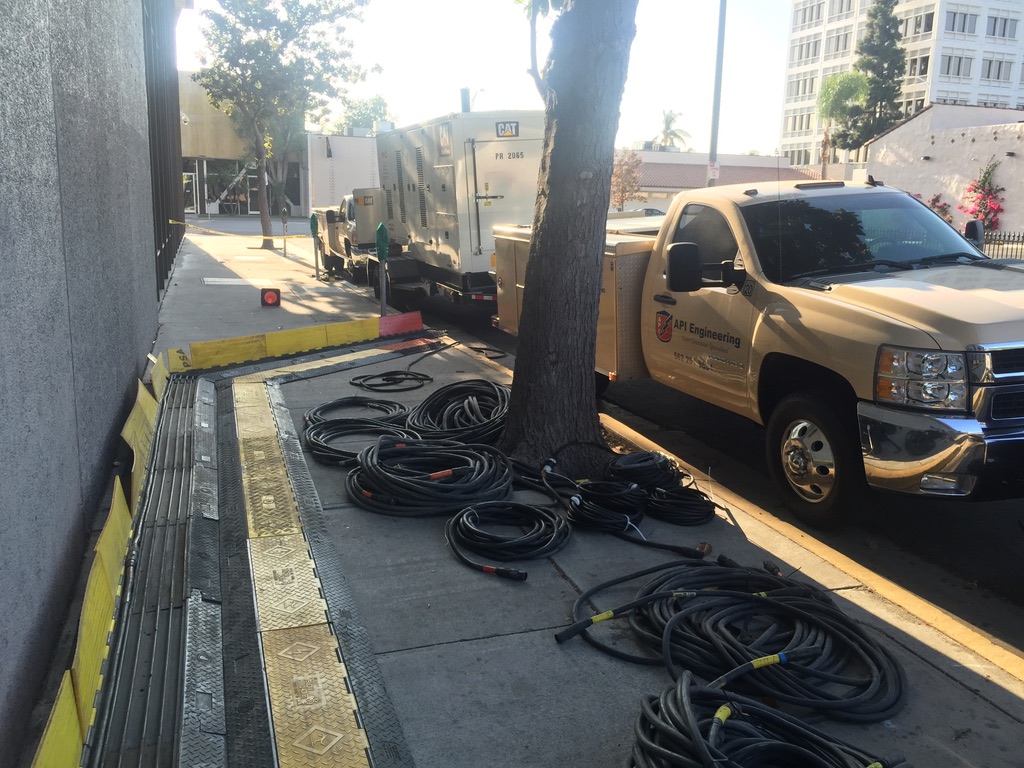 Bundles of thick black cables scattered around a sidewalk next to a parked pickup truck
