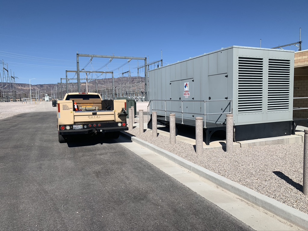 Cream-colored pickup truck parked next to a fixed, outdoor generator unit