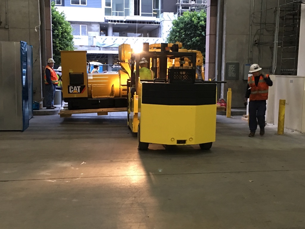 Yellow lift truck pulling a big yellow CAT generator into a warehouse