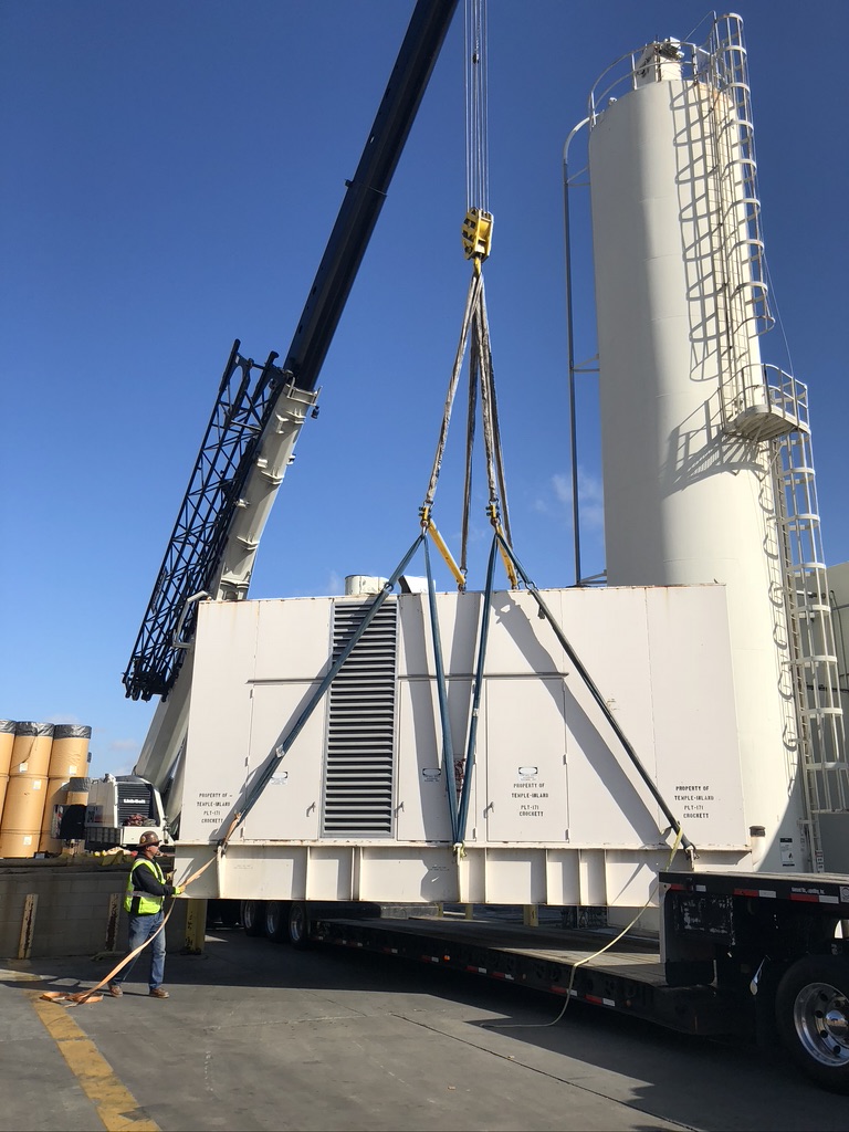 Huge white generator being lifted up using a rig equipment near white round towers