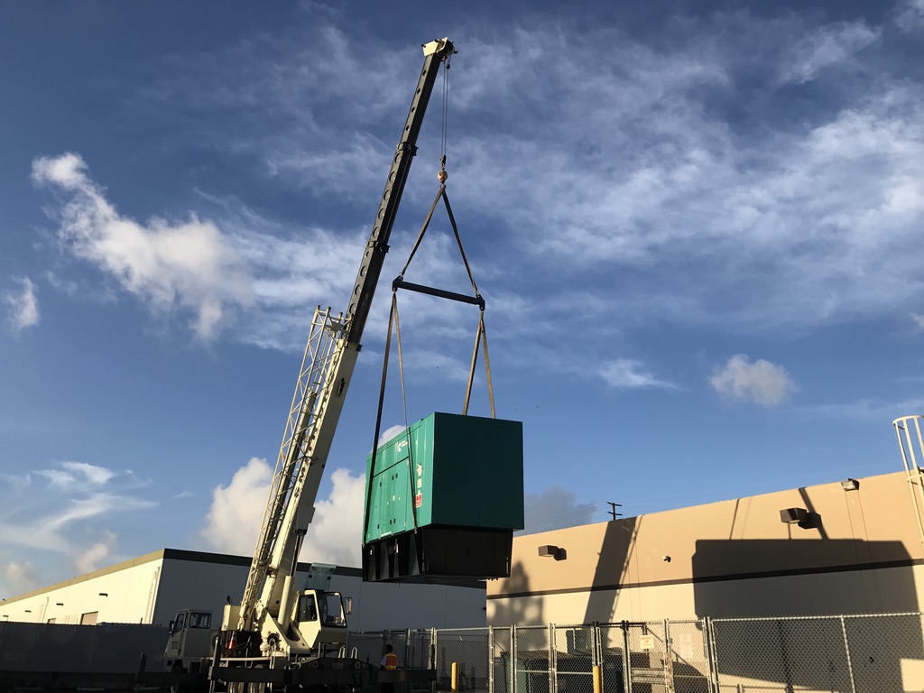 Pulley rig truck lifting up a big green generator in a spacious warehouse lot