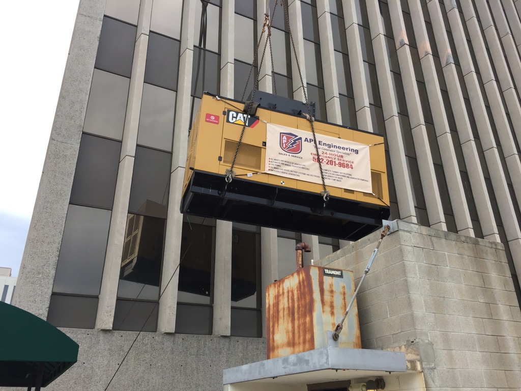 Yellow rectangle CAT generator being hoisted up a building using black ropes