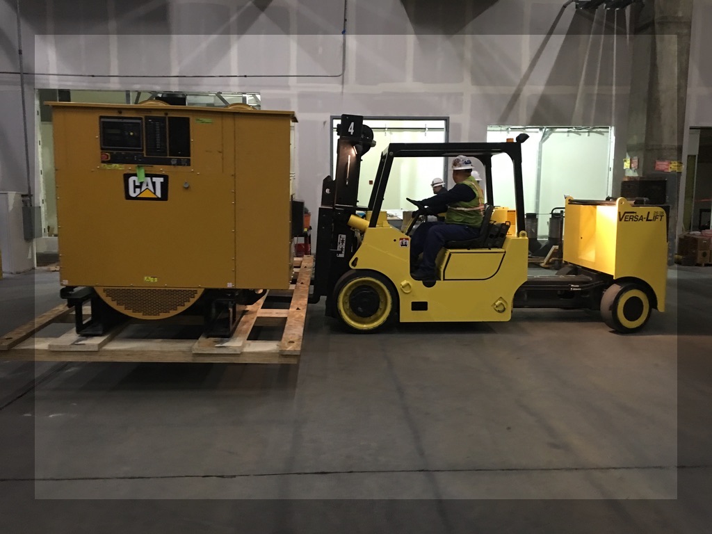 Forklift carrying a wooden platform that contains a big yellow CAT generator