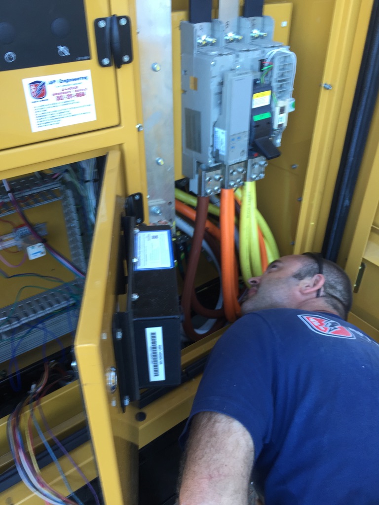 Guy in a black shirt inspecting the colorful cables of a yellow generator’s control panel
