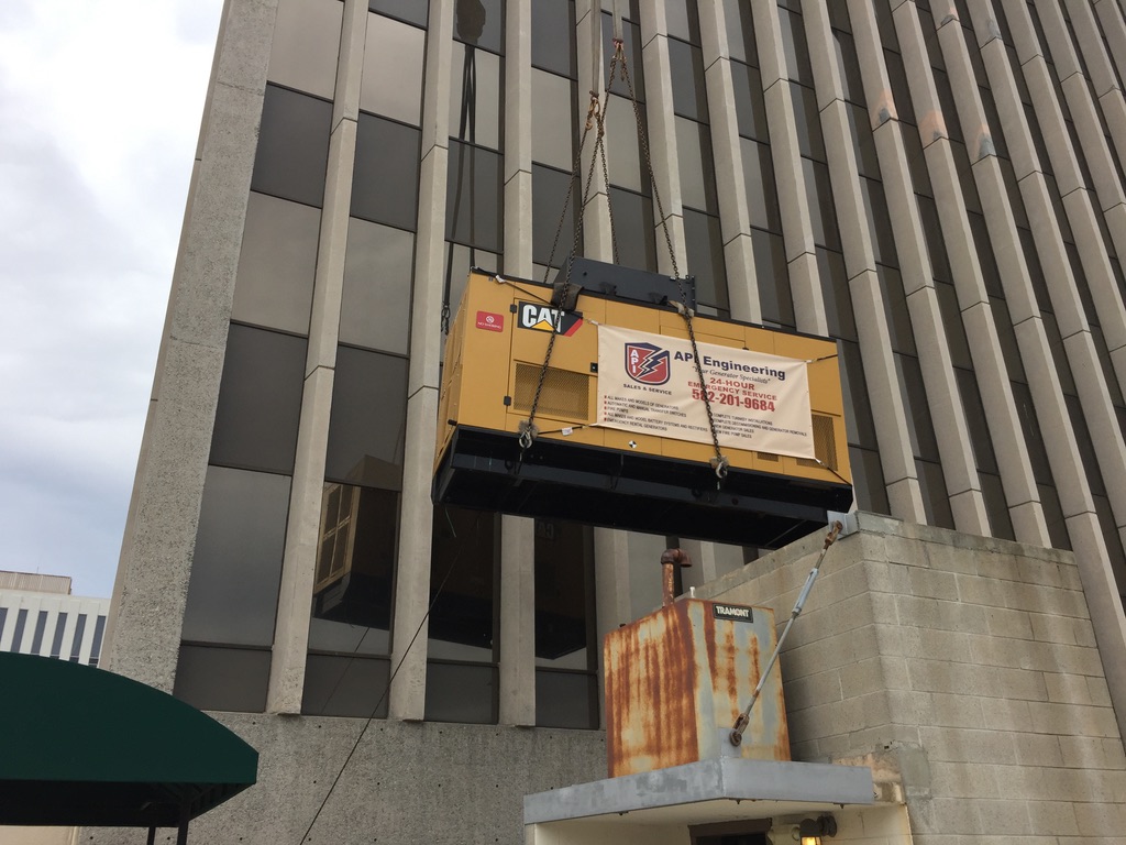 Yellow rectangle CAT generator being lifted up a building using black ropes