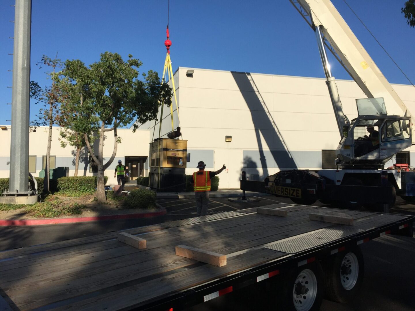 Yellow generator being lifting away from a white building using a white lift truck 